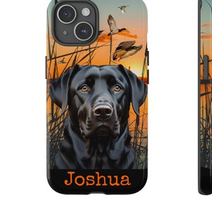 May include: A black phone case featuring a black Labrador Retriever with ducks flying in the background. The case has an orange and yellow sunset design and the name "Joshua" in orange text.
