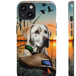 May include: A white Labrador Retriever dog with a green-headed duck in its mouth. The dog is standing in front of a sunset over a lake. The background is a silhouette of trees and reeds.