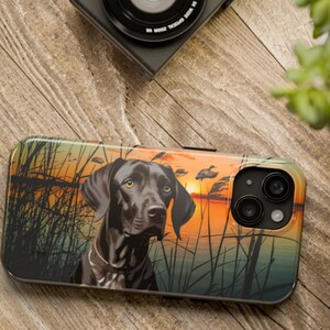 May include: A black and brown phone case with a hunting dog and a sunset scene. The case has a camera lens cutout.