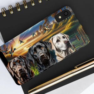 May include: Three Labrador Retriever dogs in a scenic landscape with ducks flying overhead. The dogs are black, brown, and white. The background features a sunset, trees, and water.
