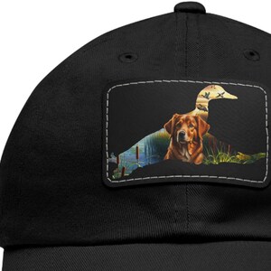 May include: Black baseball cap with a patch featuring a brown dog and a silhouette of a duck in a pond setting.