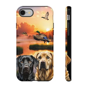 Puede incluir: Un labrador negro y un labrador marrón mirando a la cámara. Los perros están frente a una escena de puesta de sol con patos volando sobre un lago.