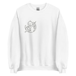 Pode incluir: Camisola branca com gola redonda e mangas compridas. Um pequeno desenho a preto de uma figura estilizada com uma espada está no peito esquerdo. A camisola tem uma etiqueta na gola.