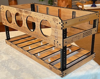 May include: A two-tiered wooden shelf with a light brown finish and black accents. The shelf features circular cutouts, engraved hieroglyphs, and the text "Rameses II". The structure is supported by black metal posts and includes white pegs.