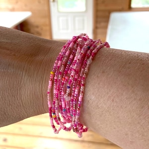 Op de afbeelding: Een meerstrengige armband gemaakt van roze en witte kralen. De armband is gelaagd en heeft een delicate, vrouwelijke uitstraling.
