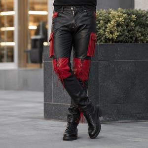Puede incluir: Una camiseta negra de manga corta combinada con pantalones de cuero negro que presentan bolsillos cargo laterales rojos y paneles con cordones rojos en los muslos. Los pantalones incluyen una cremallera frontal y botas de cuero negro.