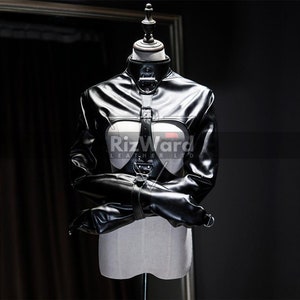 May include: A black leather-look straightjacket garment featuring a high collar, long sleeves with buckled straps, and a central vertical harness strap with metal hardware. The chest area has a cutout design, and the text RizWard LEATHER LTD is visible.