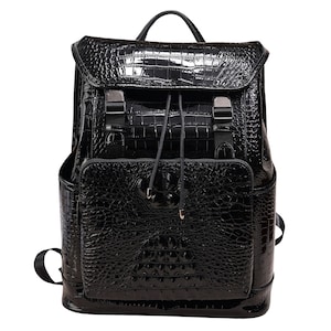 Könnte beinhalten: Ein schwarzer Rucksack mit glänzender Krokodilleder-Textur. Die Tasche hat einen Klappenverschluss mit Metallschnallen, einen Kordelzug und einen oberen Griff. Sie hat eine Vordertasche und eine Seitentasche.