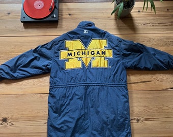 May include: A navy blue long-sleeved jacket with a large yellow "M" on the back. The "M" is outlined in white and has the word "MICHIGAN" written across the top in yellow.