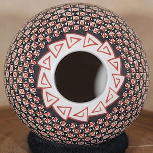 May include: A white ceramic pot with a black and red geometric design. The pot is round in shape and has a wide opening at the top.