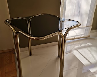 May include: A gold metal side table with a dark glass top. The table has a unique, curved design and four legs.