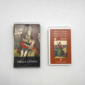 May include: A deck of Sibilla Gitana fortune-telling cards featuring a box with an illustration of two people embracing under a tree and a single card with a brown border, the text Sibilla Gitana, Sibilla Gitana, and Sibila Cigana, and a small image.
