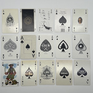 May include: A collection of Ace playing cards with various designs. The cards feature the Ace of Spades, Clubs, Diamonds, and Hearts. Some cards have illustrations, while others have company logos. The cards are arranged on a white surface.