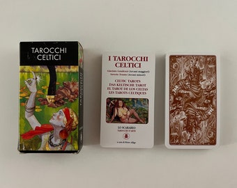 May include: A box of Celtic Tarot cards with a green and brown illustration of a woman holding a glowing orb. The box is labelled "Tarocchi Celtici" and the text "Celtic Tarots, Das Keltische Tarot, El Tarot de los Celtas, Les Tarots Celtiques" is printed on the box. The box is next to a single card from the deck, which features a brown illustration of a figure sitting on a throne.