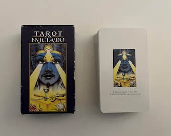 May include: Tarot del Iniciado deck box and card featuring a blue and yellow illustration of a person with a third eye and a golden headband. The card has a yellow background with a goblet, a sword, and a staff.