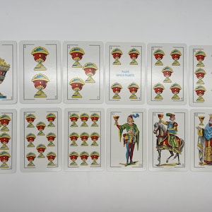 May include: A set of 12 playing cards featuring a variety of images, including cups, knights, and a king. The cards are numbered 1 through 12 and are part of a traditional Spanish deck.