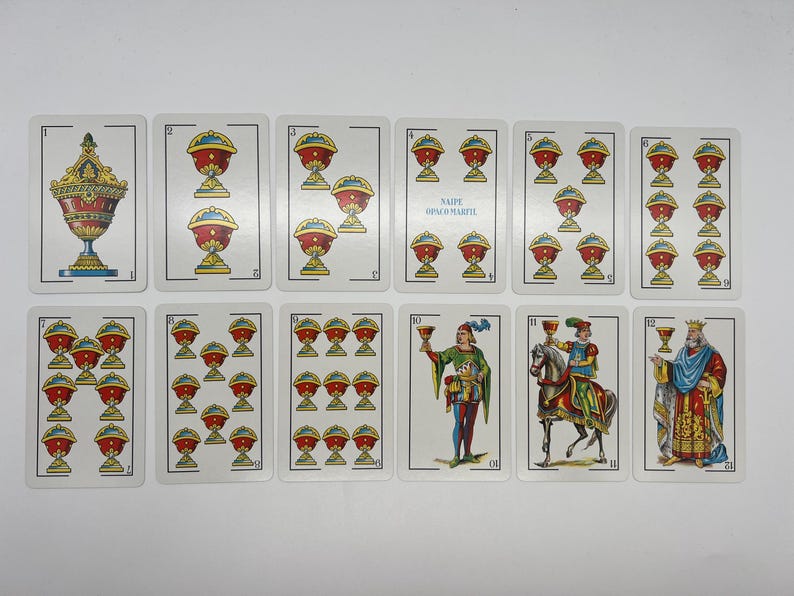 May include: A set of 12 playing cards featuring a variety of images, including cups, knights, and a king. The cards are numbered 1 through 12 and are part of a traditional Spanish deck.