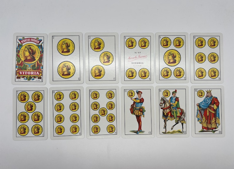 May include: A set of 11 playing cards featuring illustrations of people, animals, and coins. The cards are white with red and black text. The text on the cards includes "Victoria" and "N.&ordm; 87."