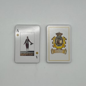 May include: Two playing cards on a white surface. One card shows a man in historical attire, the Ace of Spades. The other card features a crest with the text "Ayuntamiento de Madrid".