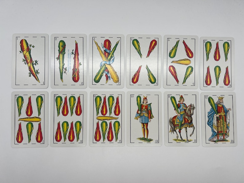 May include: A set of 12 playing cards featuring a variety of designs, including swords, cups, and coins. The cards are in a traditional Spanish style with colorful illustrations and ornate borders.