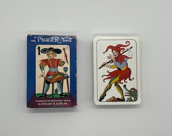 May include: The Prager Tarot card deck box with a blue background and a picture of the Magician card. The Magician is wearing a red and gold costume and holding a wand. The card number 1 is visible in the top left corner. The box has the text "The Prager Tarot" and "Complete with Instructions by Stuart R. Kaplan" printed on it.