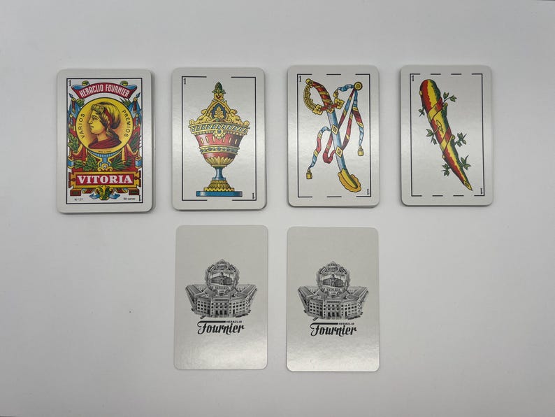 May include: A set of playing cards featuring a variety of designs, including a woman's portrait, a vase, a sword, and a vegetable. The cards are white with black borders and feature the text "Victoria" and "Fournier".