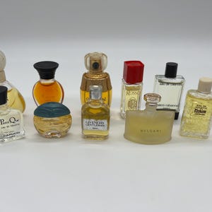 Peut inclure: Une collection de flacons de parfum miniatures de différentes formes et tailles. Les flacons présentent des bouchons et des étiquettes de couleurs différentes, certains contenant du liquide visible. Les parfums sont exposés sur une surface blanche.