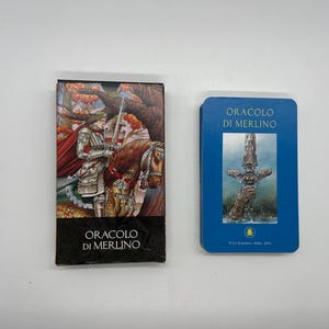 Könnte beinhalten: Ein Orakelkarten-Deck mit dem Titel "ORACLO DI MERLINO" mit blauem Kartendesign. Die Kartenbox zeigt eine Illustration eines Ritters zu Pferd. Die Karten haben einen blauen Hintergrund mit einer Schwertillustration.