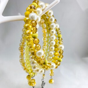 May include: A set of four bracelets featuring yellow and white beads. The bracelets are layered and have a dangling charm.