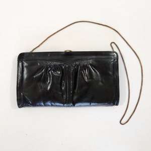 May include: A black leather clutch purse with a gold chain strap. The purse has a textured, quilted design.