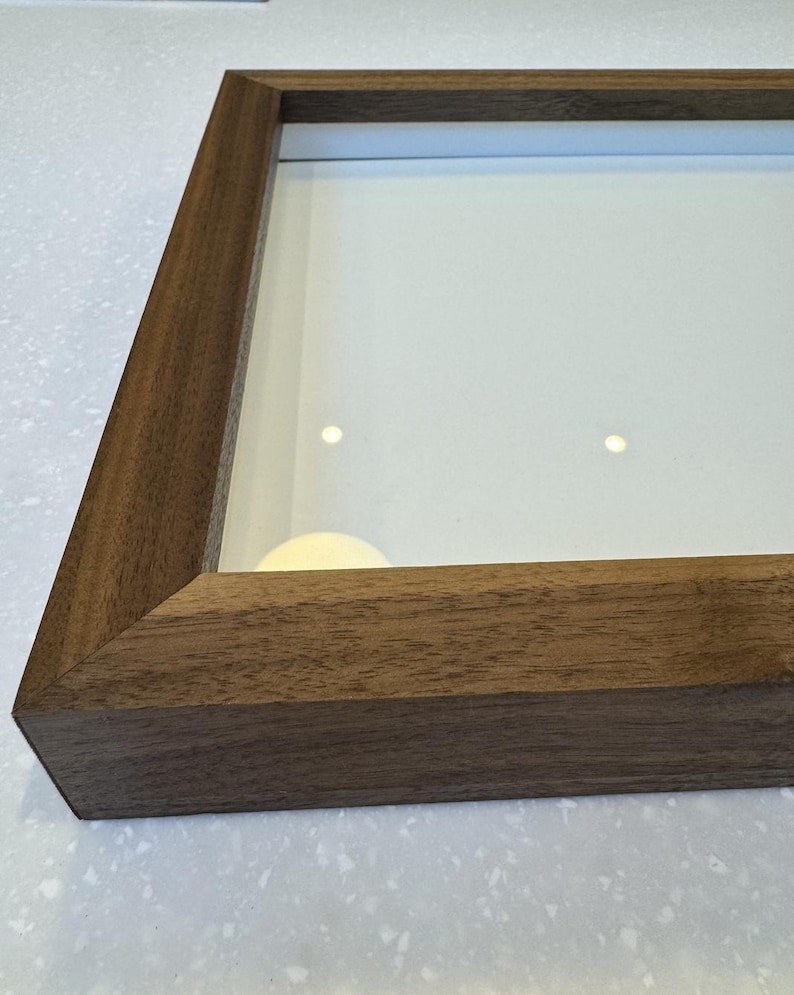 May include: A rectangular wooden picture frame with a glass pane. The frame is made of dark brown wood with visible grain. The glass pane is clear, and the frame is empty.