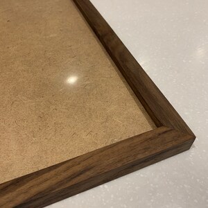 May include: A close-up of a dark brown wooden picture frame with a light brown cardboard backing.