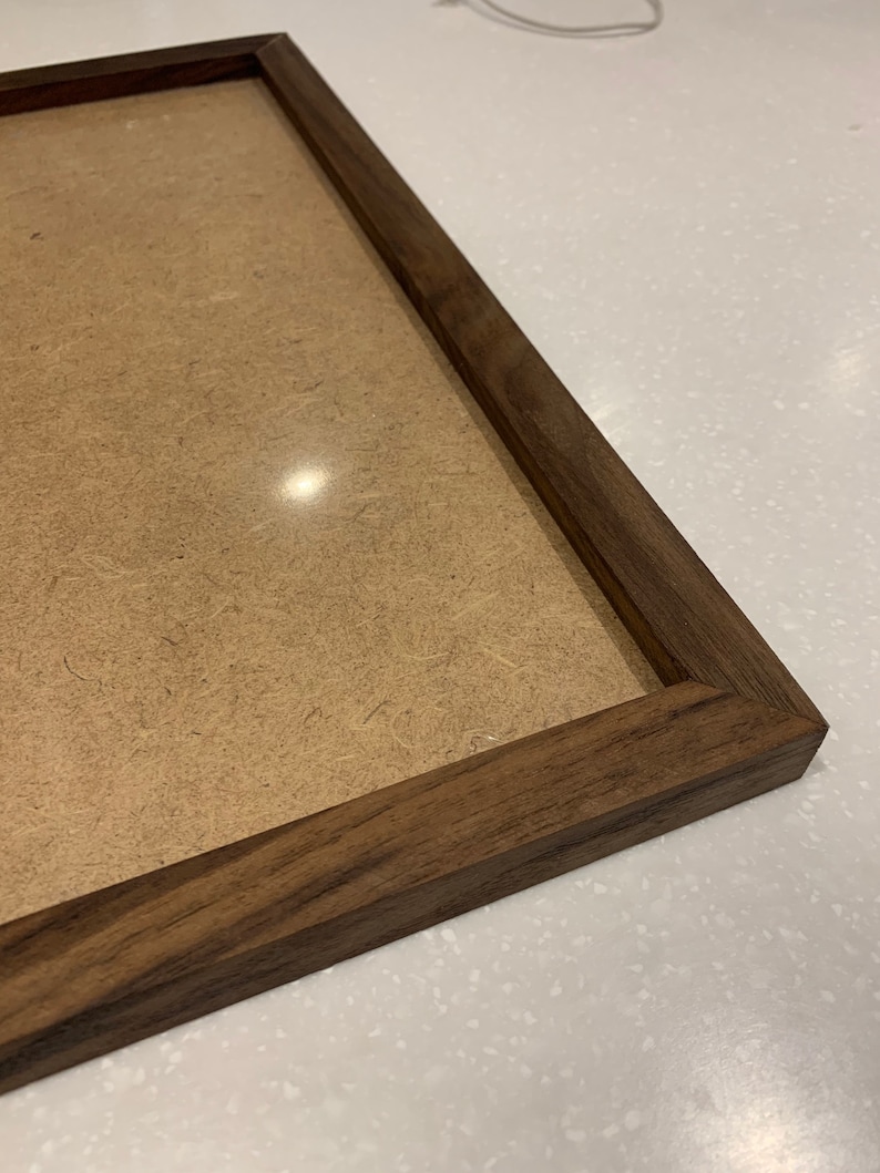 May include: A close-up of a dark brown wooden picture frame with a light brown cardboard backing.