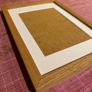 May include: A rectangular wooden picture frame with a white mount and a brown backing. The frame is made of light brown wood and has a simple, classic design. The frame is designed to hold a photograph or artwork.