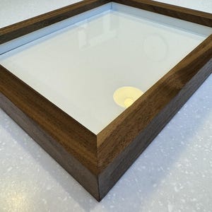 May include: A dark brown wooden picture frame with a clear glass insert. The frame has a simple, clean design.