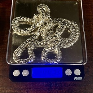 May include: A gold chain necklace on a digital scale, the scale reads 104.21. The scale is black with a blue digital display and has buttons labeled "M", "PCS", and "T". The scale is labeled "AMIR".