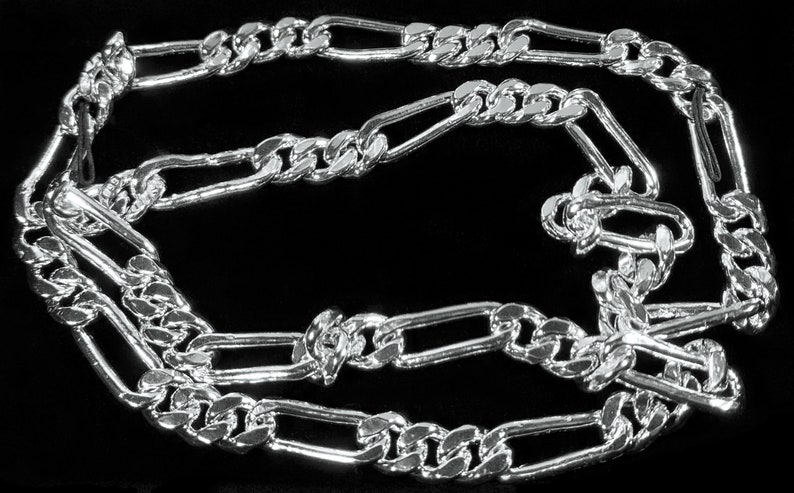 May include: A silver Figaro chain necklace with a box chain design. The chain is made of interlocking oval and round links.