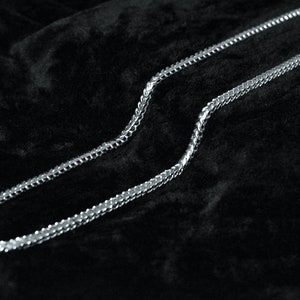 May include: A silver chain necklace on a black velvet background.