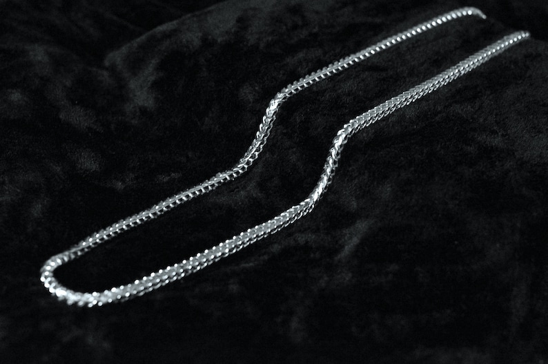 May include: A silver chain necklace on a black velvet background.