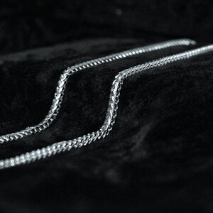 May include: Three silver chains lay on a black velvet surface. The chains are made of small, linked metal pieces.