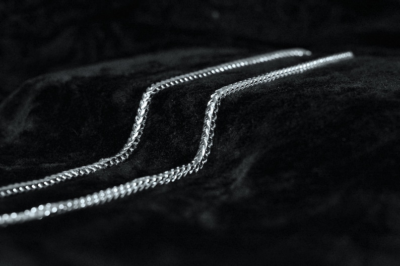 May include: Three silver chains lay on a black velvet surface. The chains are made of small, linked metal pieces.