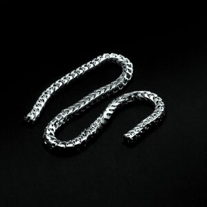 May include: A silver chain necklace with a Cuban link style. The chain is made of metal and has a shiny finish.