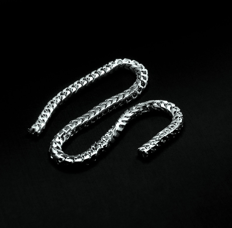 May include: A silver chain necklace with a Cuban link style. The chain is made of metal and has a shiny finish.