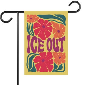 May include: A garden flag with a yellow background featuring red and orange flowers and green leaves. The words "ICE OUT" are in purple, retro-style lettering. The flag is mounted on a black metal stand.