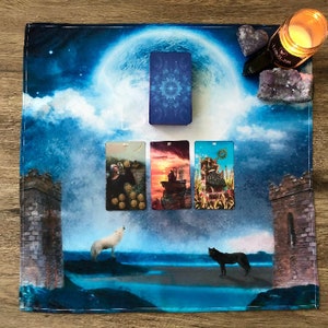 May include: Tarot card reading spread on a blue and white fabric with a full moon and clouds. The cards are The World, The Tower, The Chariot, and The Empress.