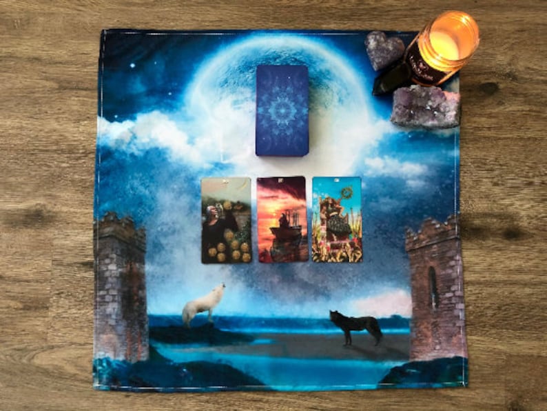 May include: Tarot card reading spread on a blue and white fabric with a full moon and clouds. The cards are The World, The Tower, The Chariot, and The Empress.