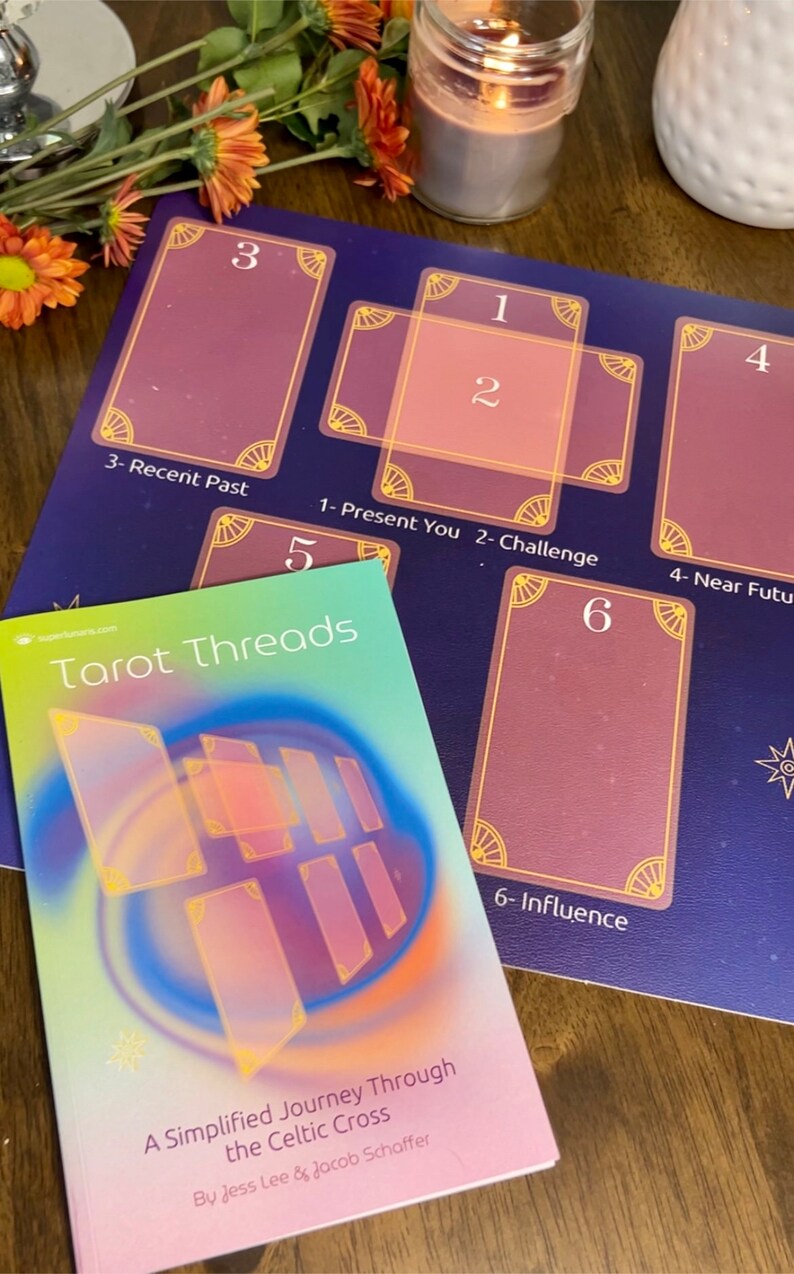 May include: A Celtic Cross tarot spread layout with six numbered cards, a book titled "Tarot Threads: A Simplified Journey Through the Celtic Cross" by Jess Lee & Jacob Schaffer, and a candle in the background.