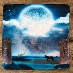 May include: A blue and white watercolor painting of a full moon with two wolves howling at each other. The wolves are silhouetted against a dark blue sky with clouds. The moon is in the center of the painting and is surrounded by a dark blue sky with clouds. The wolves are on either side of the moon and are facing each other. The painting is framed in a dark blue frame.