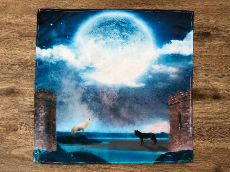May include: A blue and white watercolor painting of a full moon with two wolves howling at each other. The wolves are silhouetted against a dark blue sky with clouds. The moon is in the center of the painting and is surrounded by a dark blue sky with clouds. The wolves are on either side of the moon and are facing each other. The painting is framed in a dark blue frame.