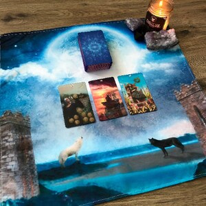 May include: A blue and white tarot cloth with a full moon, clouds, and two towers. Four tarot cards are laid out on the cloth, and a white wolf and a black wolf are howling at the moon. There is a candle and crystals on the top right corner of the cloth.